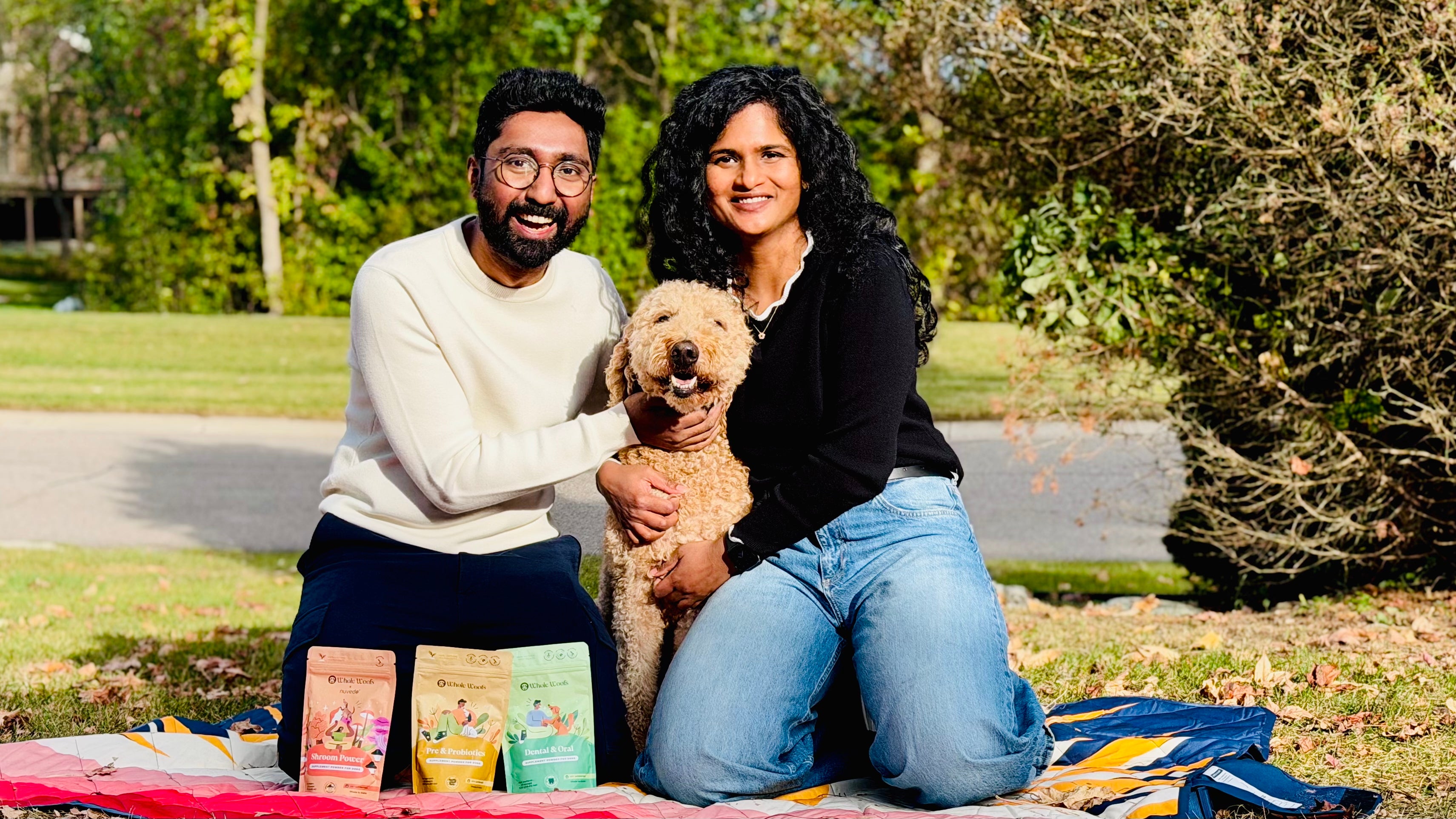 Two people with a dog on a blanket in a park